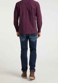 Koszula w kratę z długim rękawem w ciemnoczerwonym i granatowym kolorze, w połączeniu z niebieskimi dżinsami. Brązowe botki z fakturowanym wykończeniem i widoczną jasną podeszwą.