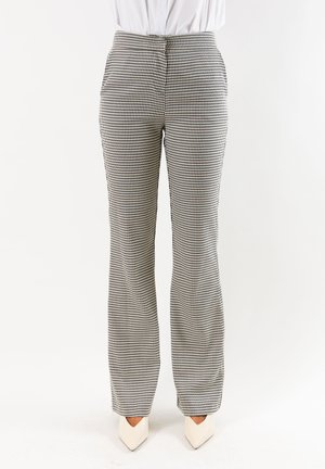 Donna che indossa pantaloni dritti a vita alta con motivo pied-de-poule bianco e nero e scarpe bianche con punta affilata.