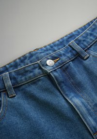 Blugi din denim de culoare albastră medie, cu închidere cu buton argintiu, cusături în contrast și o etichetă brodată la talie cu o ușoară decolorare.