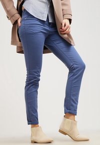 Pantalons slim-fit bleus en mélange de coton, dotés d'une texture lisse et de détails cousus. Associés à des bottines beiges à la cheville.