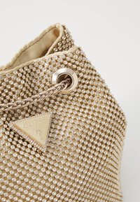 Borsa a secchiello metallica d'oro con superficie testurizzata e piccoli strass incastonati. Presenta una catena argento e un accento con logo triangolare.