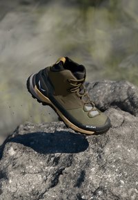 Zielono-czarne buty trekkingowe z szarymi akcentami, syntetyczna cholewka, wysokie wsparcie kostki i solidna podeszwa, zaprezentowane na kamienistej powierzchni.