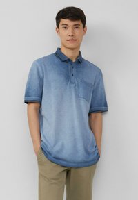 Koszulka polo z krótkim rękawem w gradientowych odcieniach niebieskiego, wykonana z mieszanki bawełny, z kołnierzykiem, zapięciem na dwa guziki oraz kieszonką na lewej piersi.