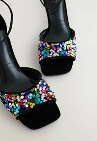 Sandali con tacco neri, dotati di una larga cinturino in paillettes con paillettes multicolori di varie dimensioni, accentuato da una morbida texture nera.