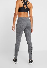 Conjunto deportivo con un sujetador deportivo negro y leggins grises. Los leggins tienen una apariencia texturizada y un acento negro a lo largo del costado.