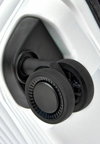 Rueda negra unida a un cuerpo de equipaje plateado texturizado, con un diseño elegante y bordes redondeados, y un mango curvado para mayor movilidad.