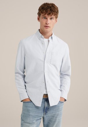 Camicia azzurro chiaro con colletto a punta, taschino sul petto singolo e maniche lunghe, abbinata a jeans in denim chiaro.