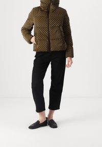 Olivengrøn dunjakke med ternet mønster, høj krave, lynlås foran og sidelommer, kombineret med sorte cropped bukser og loafers.