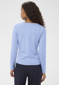 Világoskék hosszú ujjú felső kerek nyakkivágással, puha anyagból készült, sima textúrával és testhez simuló szabással.