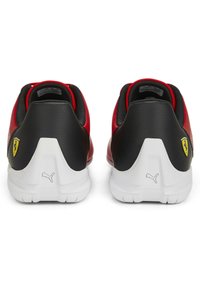 Czerwono-czarne buty sportowe z gładką skórzaną cholewką, teksturowanym czarnym piętkiem, białą podeszwą i żółtym logo Ferrari z boku.