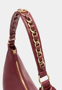 Borsa a mano in pelle bordeaux con una texture liscia, presenta un accento in catena dorata sul manico e una chiusura with zip sul lato.