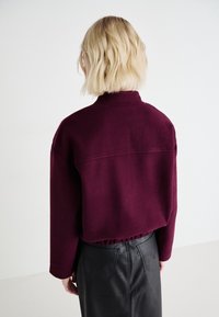 Pull court bordeaux avec col montant et épaules tombantes, associé à une jupe en cuir noire ajustée avec poches arrière.