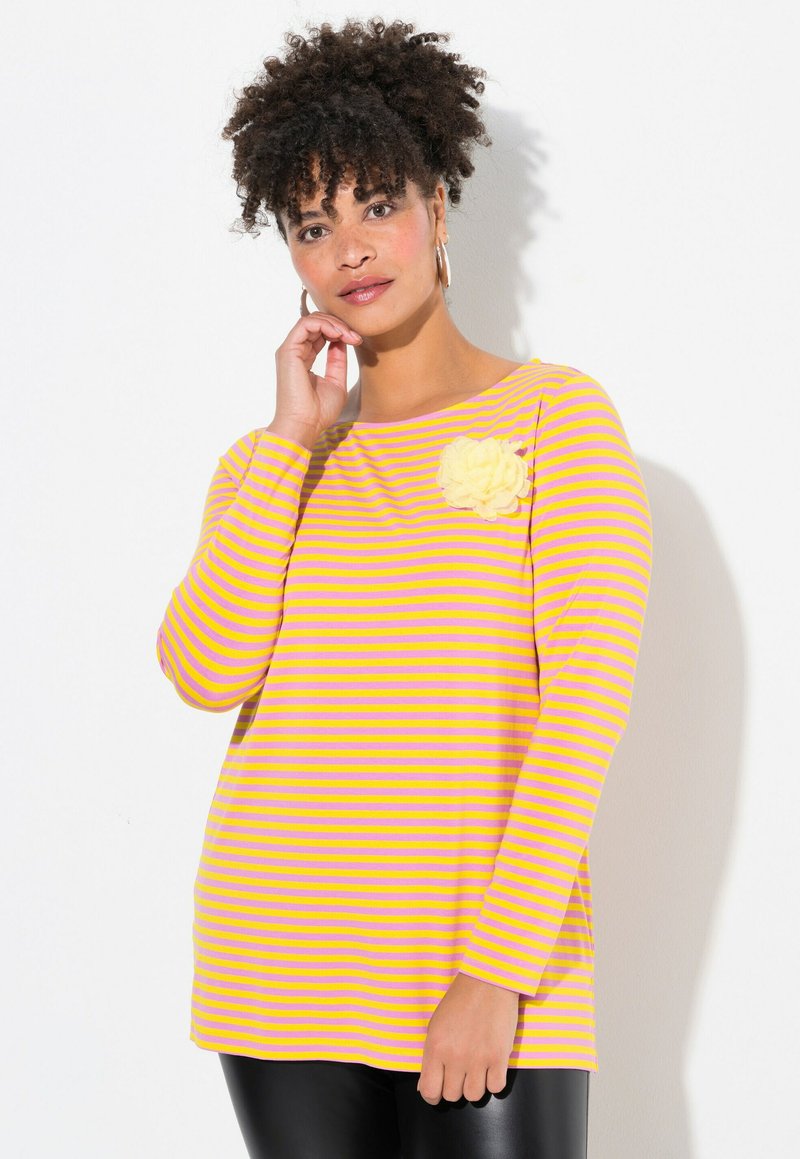 Maglietta a maniche lunghe a righe gialla e lavanda, con scollo rotondo e un'applicazione floreale in tessuto sulla spalla sinistra. Texture morbida, vestibilità comoda.