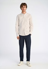 Camicia a maniche lunghe a righe beige chiaro e bianco, pantaloni slim-fit blu navy e sneakers bianche con dettagli colorati. Design minimalista con colletto.