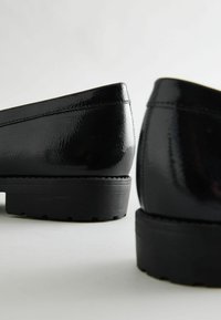 Schwarze Lackslipper mit einer glatten, glänzenden Oberfläche, ausgestattet mit einer soliden Gummisohle und einer einfachen, runden Silhouette.