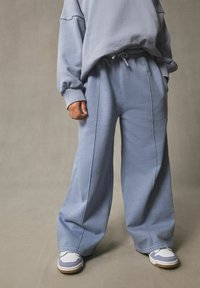 Pantalons de survêtement bleu clair, à jambes larges, avec une taille élastique et des poches latérales, associés à un haut assorti de coupe décontractée et des baskets blanches.