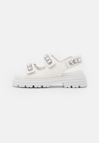 Sandales blanches matelassées avec deux sangles ajustables, ornées de strass transparents, et une semelle épaisse blanche avec un motif texturé.