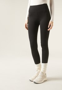 Leggings neri con vita alta, abbinati a sneakers chiare e calzini alla caviglia color crema. Texture liscia e design aderente.