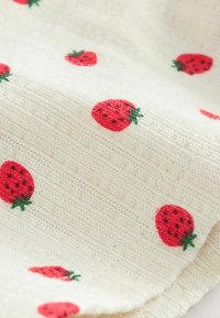Tissu blanc texturé avec un motif de petites fraises rouges aux feuilles vertes, réparties uniformément sur toute la surface.