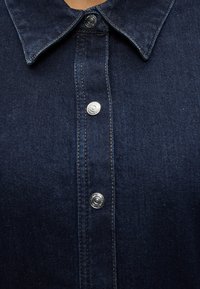 Σκούρο μπλε πουκάμισο από τζιν με μυτερό γιακά και ασημένια κουμπιά τύπου τρουκ στο μπροστινό μέρος.