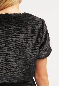 Cropped top in pelliccia nera con superficie texturizzata e ondulata, maniche corte, scollatura rotonda e senza chiusure visibili.