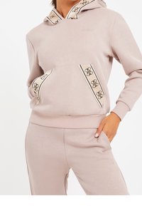 Sudadera con capucha rosa claro con ribete estampado contrastante en la capucha y los bolsillos. Tela suave, con detalles sutiles del logo y puños acanalados.