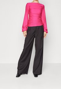 Figursydd rosa blus med rynkad textur och långa ärmar, kombinerad med högmidjade, vida svarta byxor och svarta klackstövlar.