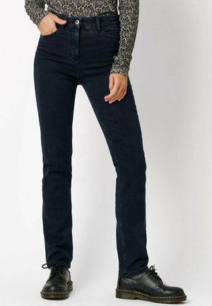 Dunkelblaue Denim-Jeans mit hoher Taille, geradem Bein, minimalen Nähten und Vordertaschen, kombiniert mit schwarzen Schnürstiefeln.