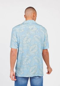 Kurzarmhemd aus hellblauem Stoff mit einem tropischen Blattmuster in Cremetönen, mit geradem Saum und weicher Textur.