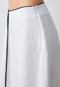 Jupe en lin blanc avec une texture lisse, dotée d'une finition noire le long de la fermeture éclair au dos. Design à silhouette droite.