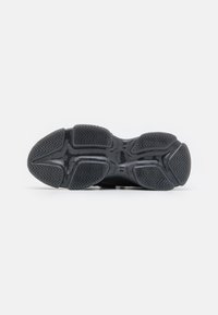 Suela de zapato deportivo negra con goma texturizada para tracción, que presenta un patrón en zigzag y una zona de entresuela suave.
