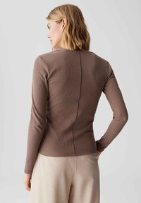 Maglietta marrone a maniche lunghe con righe, dal design aderente, caratterizzata da una cucitura centrale che scende verticalmente lungo la schiena. Texture liscia, con accenti minimi.