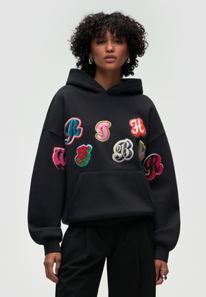 Black hoodie featuring colorful embroidered letters in various styles. The design includes a front pocket and ribbed cuffs. Soft texture.