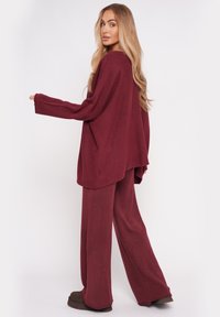 Burgundowy komplet dresowy z dzianiny, składający się z luźnej bluzki z szerokimi rękawami oraz dopasowanych spodni w szerokim kroju, zapewniający wygodny fason i miękką fakturę.
