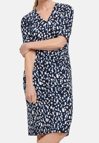 Marinblå klänning med omslagdesign, prydd med ett geometriskt mönster av vita och ljusblå rutor. Korta ärmar och strukturerad tyg.