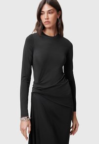 Svart långärmad klänning i slät tyg. Har en figurnära överdel med draperad midja och utsvängd kjol. Minimalistisk design utan mönster.
