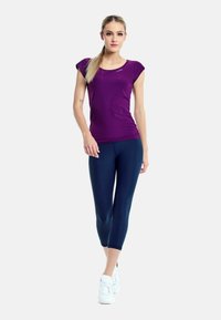 Purple cap-sleeve athletic top with a smooth texture, paired with navy cropped leggings. White sneakers complete the outfit.