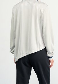 Ljust grå långärmad jacka med en slät yta, med ett tonalt randmönster och en Nike-logga på baksidan av kragen.