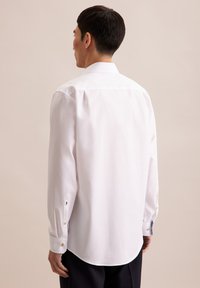 Camicia bianca con maniche lunghe, orlo arrotondato e dettagli dei bottoni a contrasto sui polsini, mostrata da dietro. Texture del tessuto liscia.