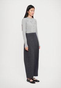 Cardigan en tricot gris avec des détails texturés, cinq boutons, associé à un pantalon large à rayures foncées taille haute et des ballerines noires.