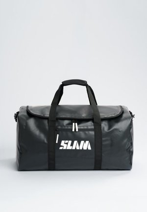 Bolsa de deporte negra con dos asas, una correa para el hombro, un bolsillo delantero con cremallera y un logotipo blanco estilizado, sobre un fondo liso y claro.