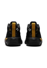 Para czarno-złotych sportowych butów widziana od tyłu, z metalicznymi złotymi logo Jumpman i białym numerem "23" na kołnierzach pięty.