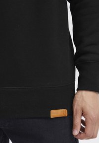 Zwarte sweatshirt met geribde manchetten en onderrand. Beschikt over een tan leren label aan de onderste linkerkant. Zachte textuur en standaard pasvorm.
