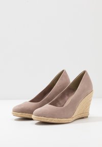 Scarpe con zeppa con una morbida tomaia in suede beige e una suola in giuta intrecciata, caratterizzate da una punta arrotondata e un design del tacco leggermente scosceso.