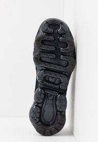 Semelle de chaussure de sport noire avec une surface en caoutchouc texturée, présentant un motif de semelle distinctif et des éléments de rembourrage.
