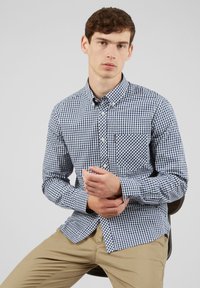Camicia a quadri blu e bianca con maniche lunghe e una tasca sul petto, realizzata in tessuto di cotone intrecciato.