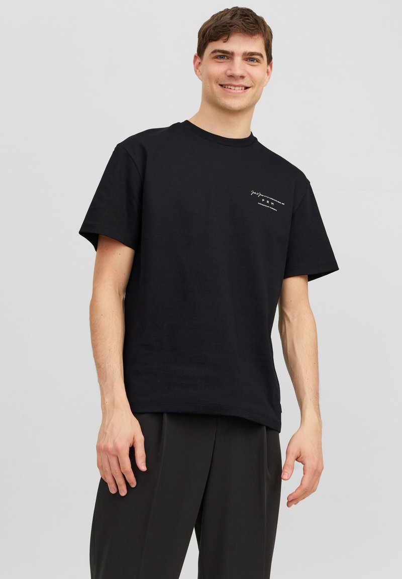 Camiseta de algodón negra con mangas cortas y cuello redondo, que presenta un pequeño gráfico blanco en el lado izquierdo. Corte recto.