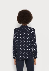 Blusa bleu navy con pois bianchi, maniche lunghe e colletto; presenta una linea dritta e un tessuto leggero e morbido.