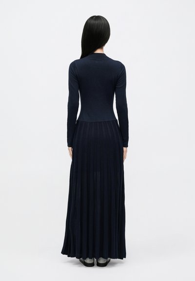 Sukienka maxi z długim rękawem w granatowym kolorze, z dopasowanym gorsetem i plisowaną spódnicą, wykonana z miękkiego, lekkiego materiału o prążkowanej fakturze.