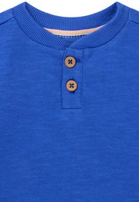 Blauwe katoenen henley-shirt met een ribbelkraag, twee bruine knopen bij de hals en een gestructureerde stof met een zachte afwerking.